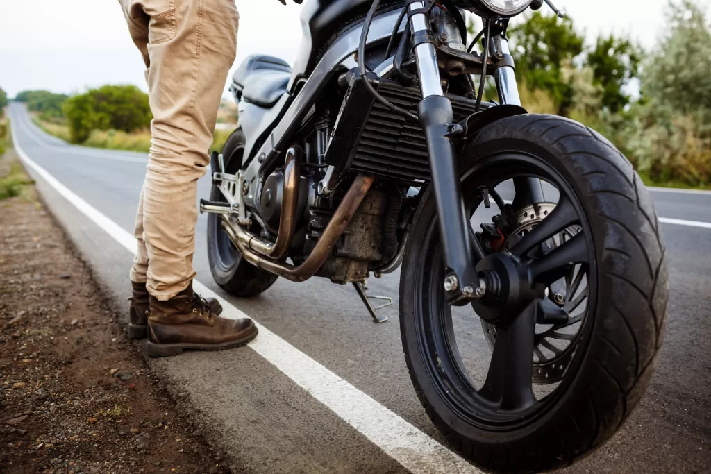 jovem bonito posando perto de sua moto na estrada rural